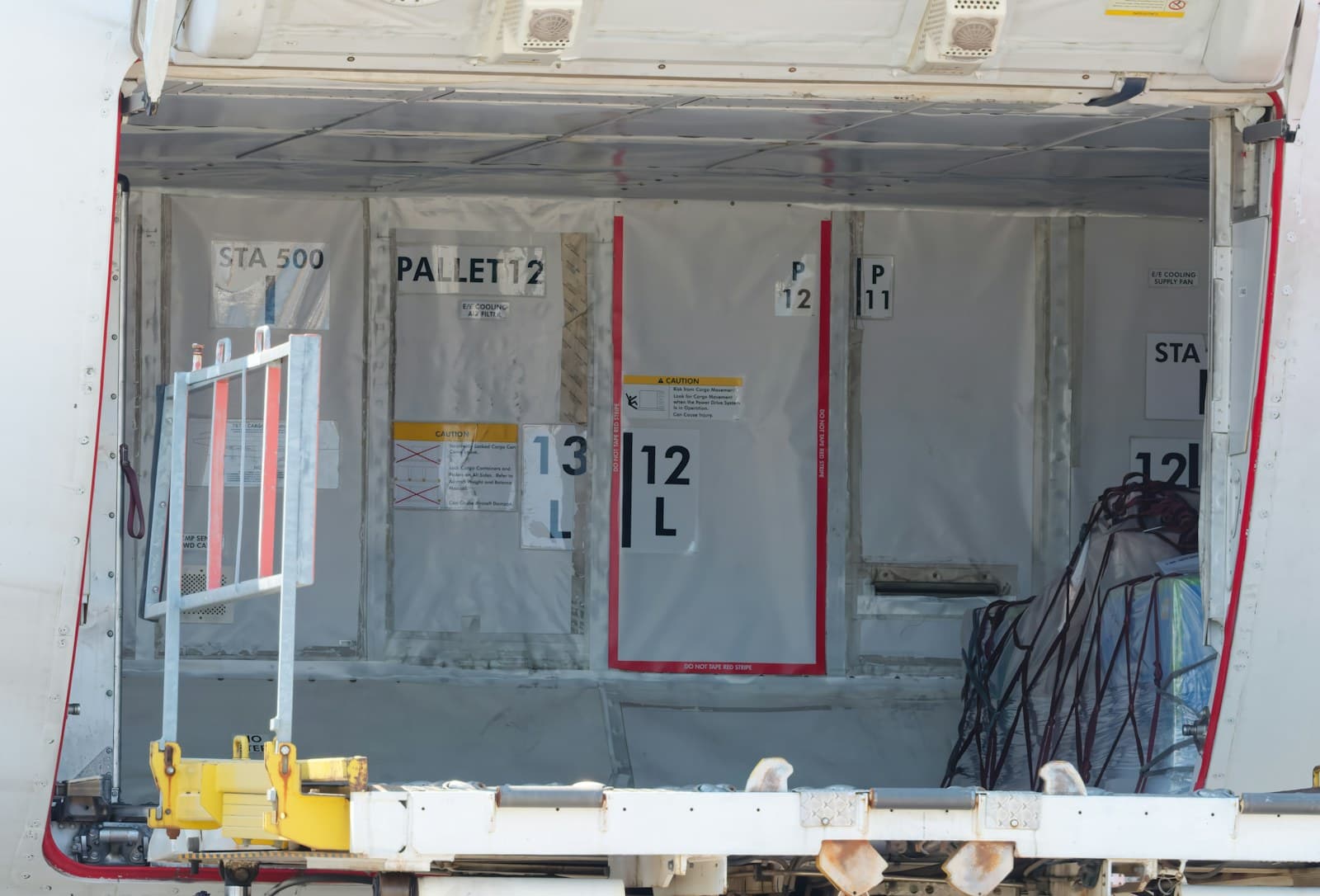 Inside an aircraft lower cargo hold showing pallet position markings and a netted pallet